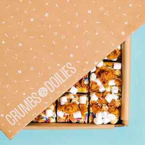 Cereal Milk Rocky Road in a Crumbs & Doilies box with marshmallows, cornflakes, and rainbow sprinkles visible.